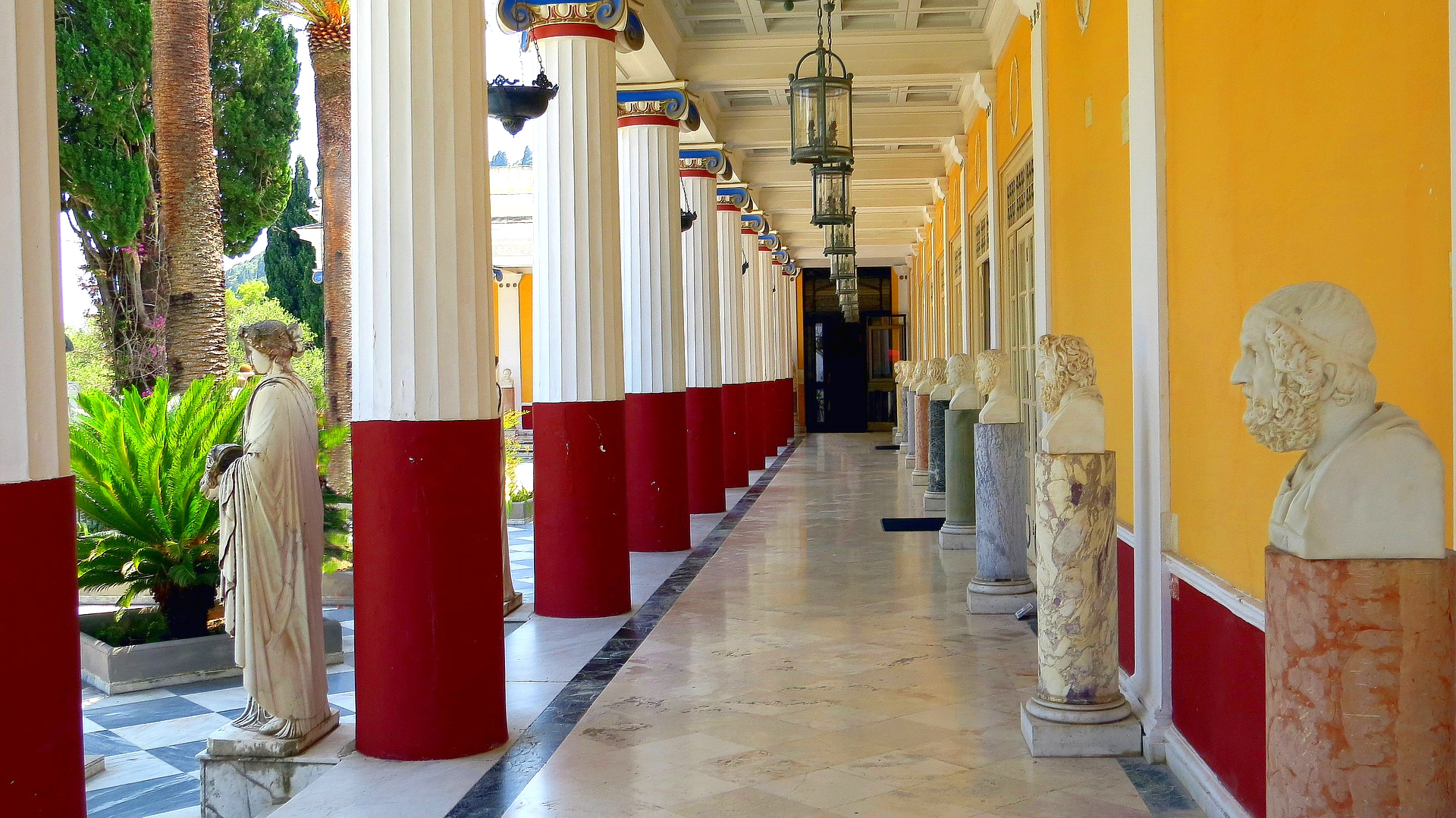 Red and yellow walls of palace. Busts land columns line the outdoor hallway.