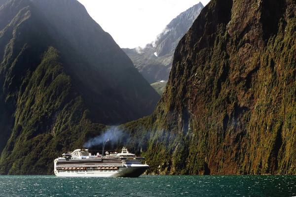 A cruise ship in the water infront of large green mountains