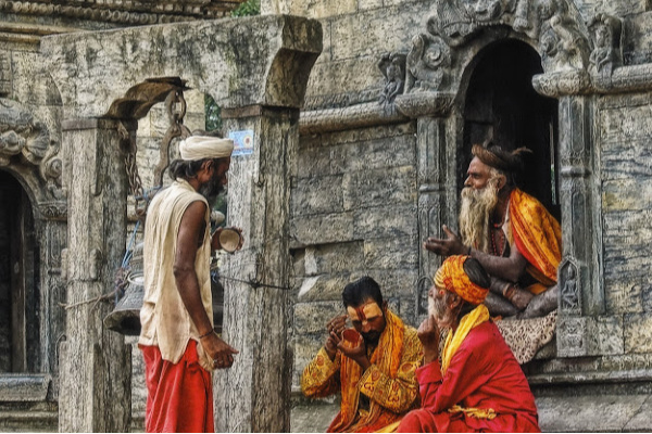 A group of Indian men in traditional clothing chatting and painting their faces outside a temple