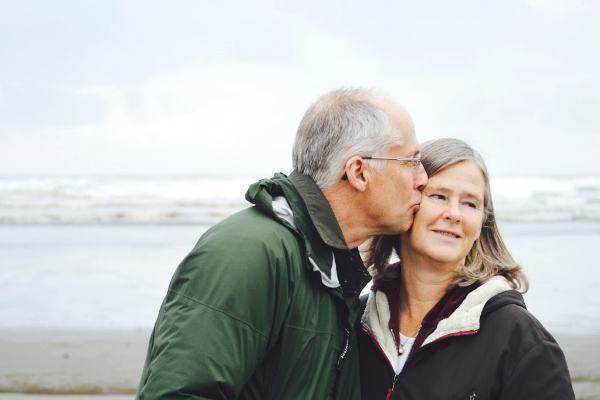 An older gentleman kissing his wife on the cheek at the beach