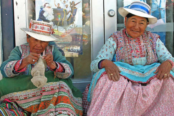 two Peruvian women in traditional clothing sitting outside a building